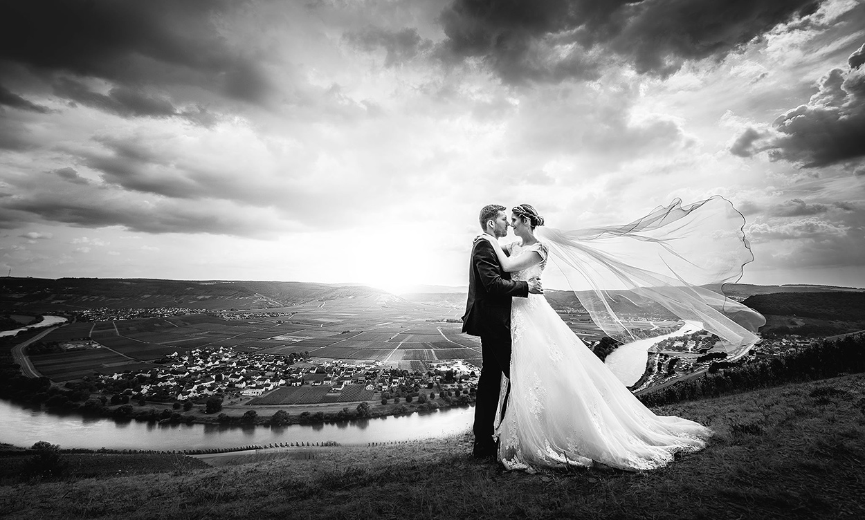 Brautpaar hoch über der Mosel als Panorama Hochzeitsfoto bei Trier mit dramatischen Wolken in schwarzweiß